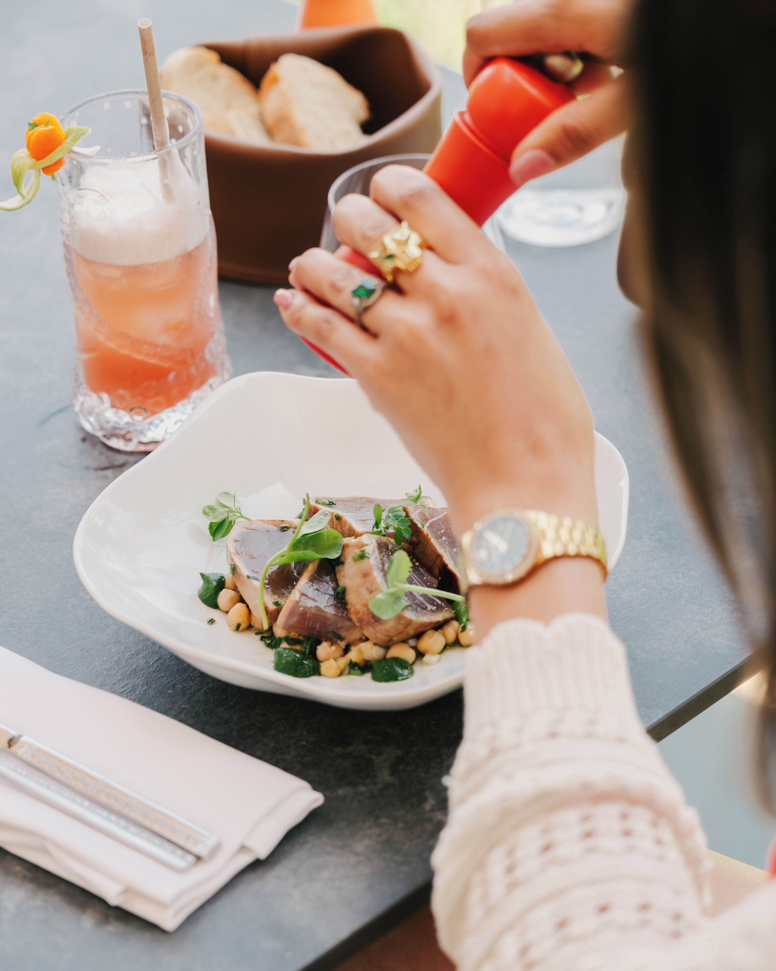 A dining table with a plate of food, a drink with a straw, and a bowl of bread.