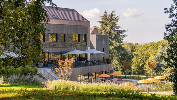 A modern building with a covered outdoor seating area, surrounded by trees and a grassy landscape. - Domaine de Dolomieu, BW Premier Collection (Dolomieu)