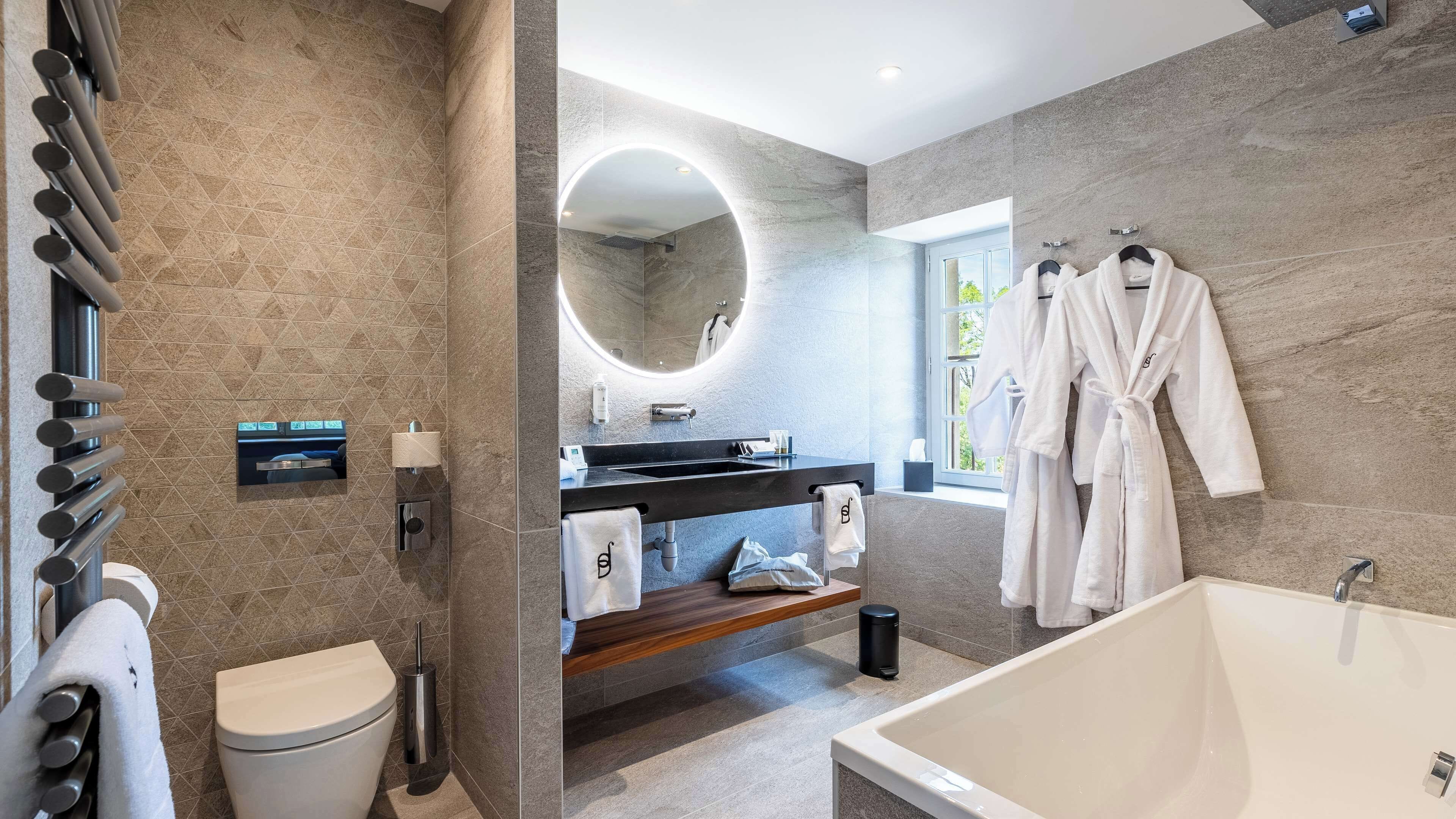 A modern bathroom with a large bathtub, a round mirror, and a vanity with a sink.