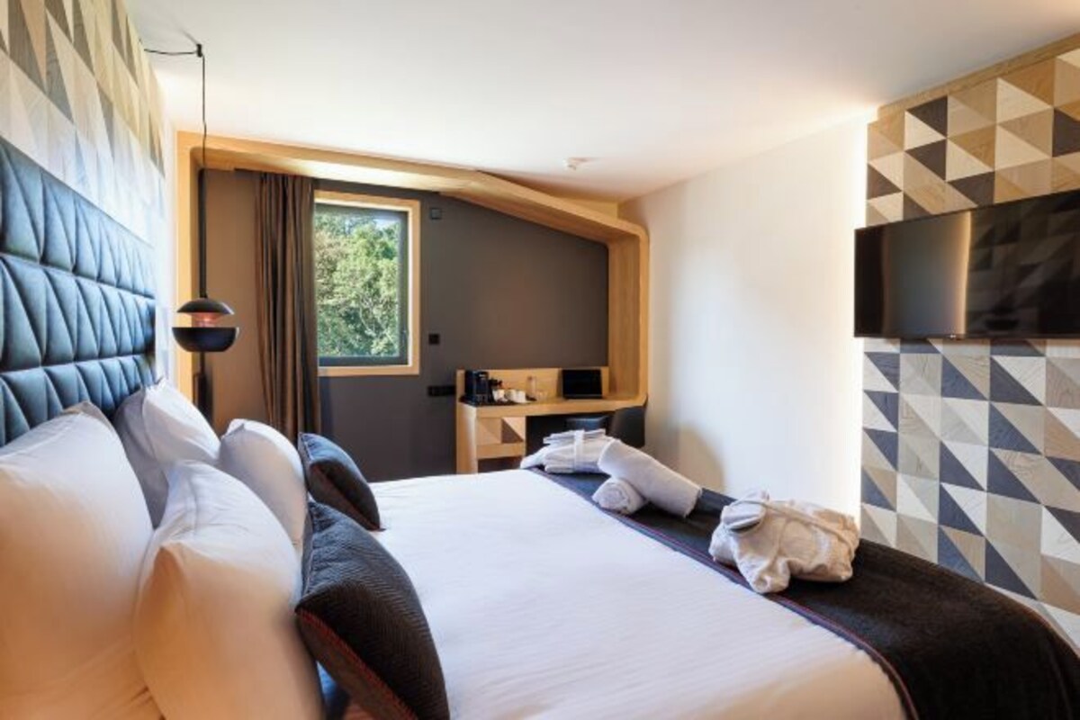 A modern hotel room with a large bed, a flat-screen TV mounted on the wall, and a small desk with a chair.