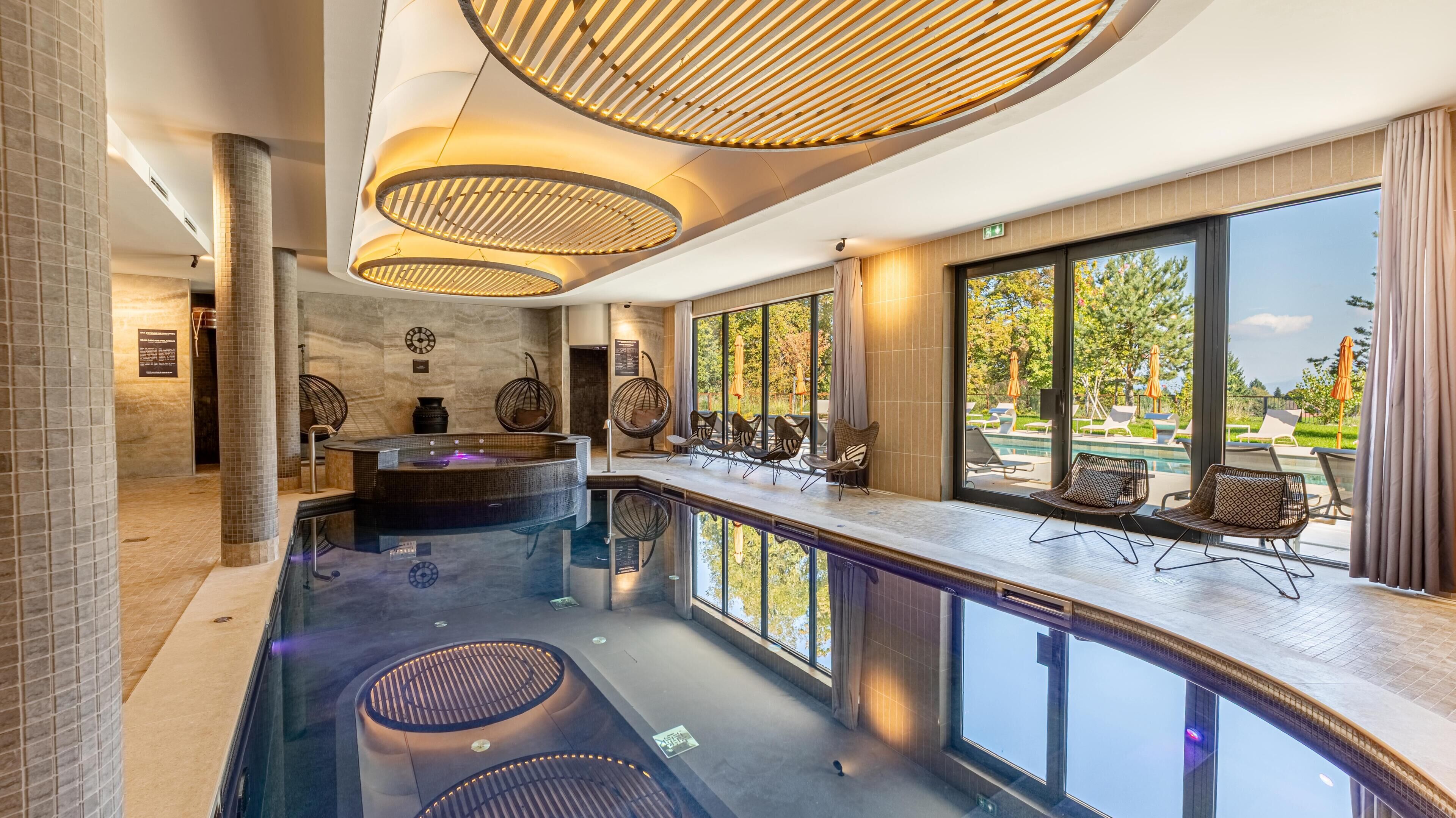 Una piscina interior moderna con un jacuzzi, sillas de descanso y vistas al exterior.