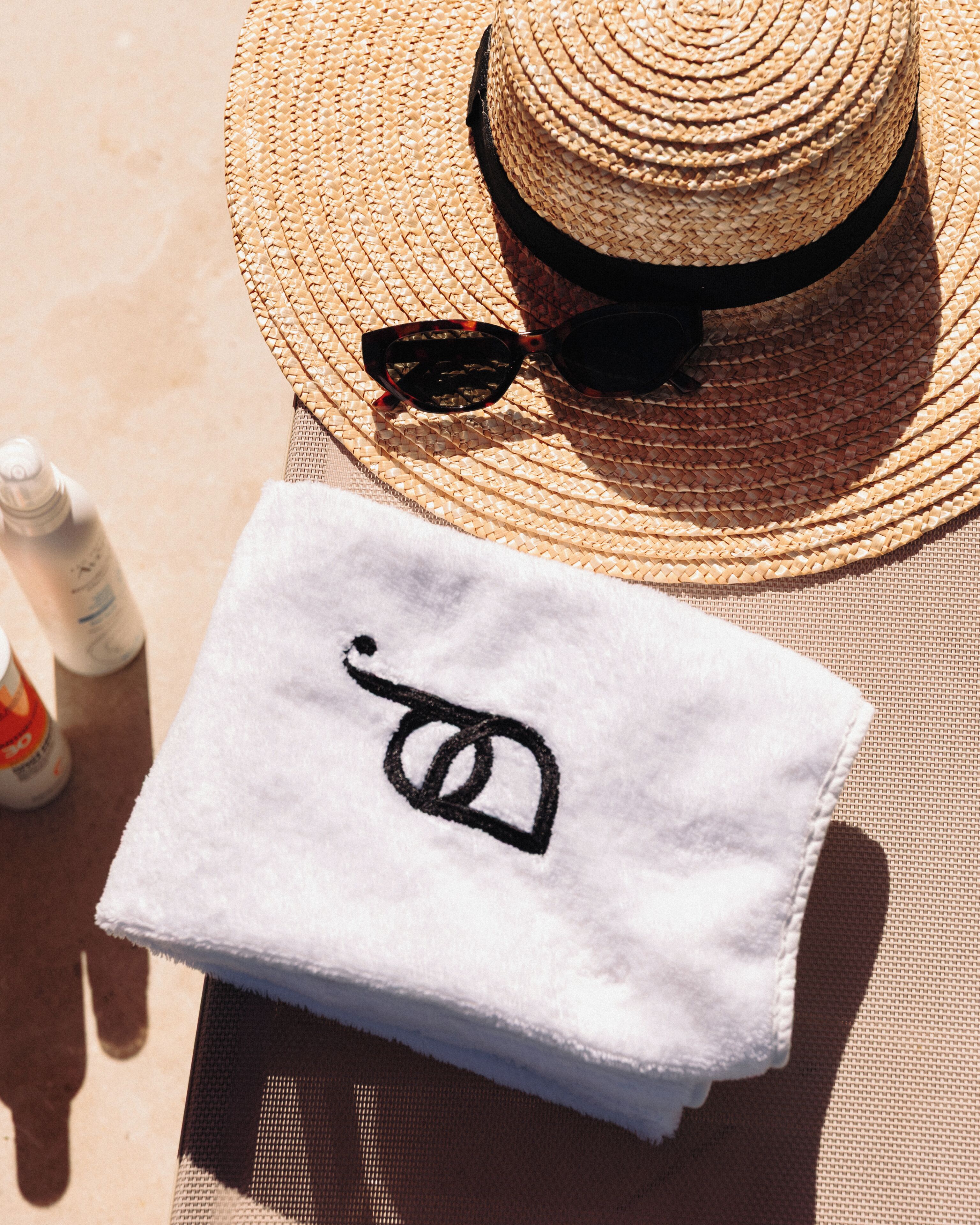 Un sombrero de paja, gafas de sol y una toalla con un logotipo sobre una superficie.