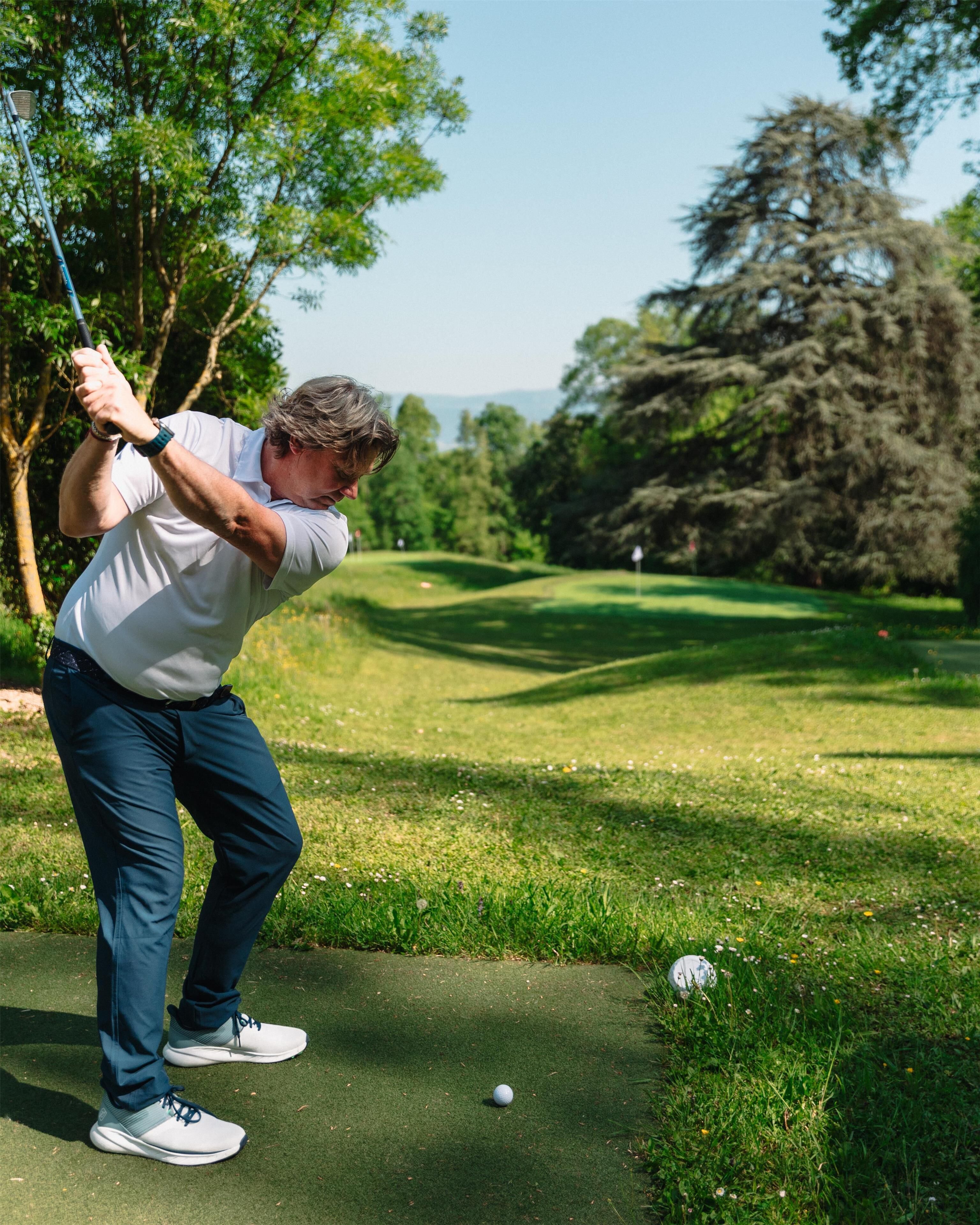 A person playing golf on a well-maintained course with trees and a clear sky in the background.
