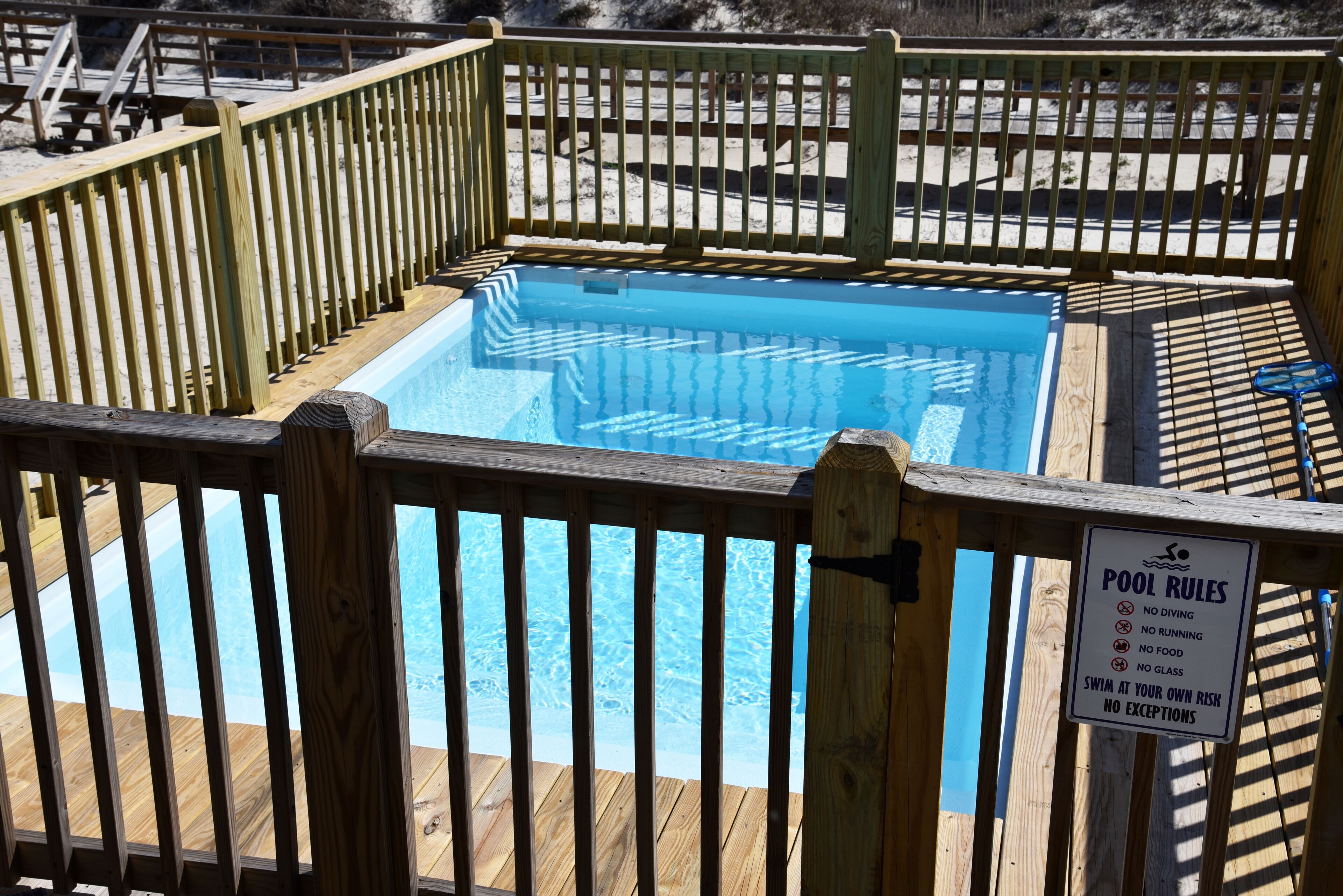 Una piscina con plataforma de madera y un cartel que enumera las normas de la piscina.