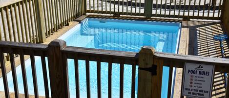 Una piscina con plataforma de madera y un cartel que enumera las normas de la piscina.