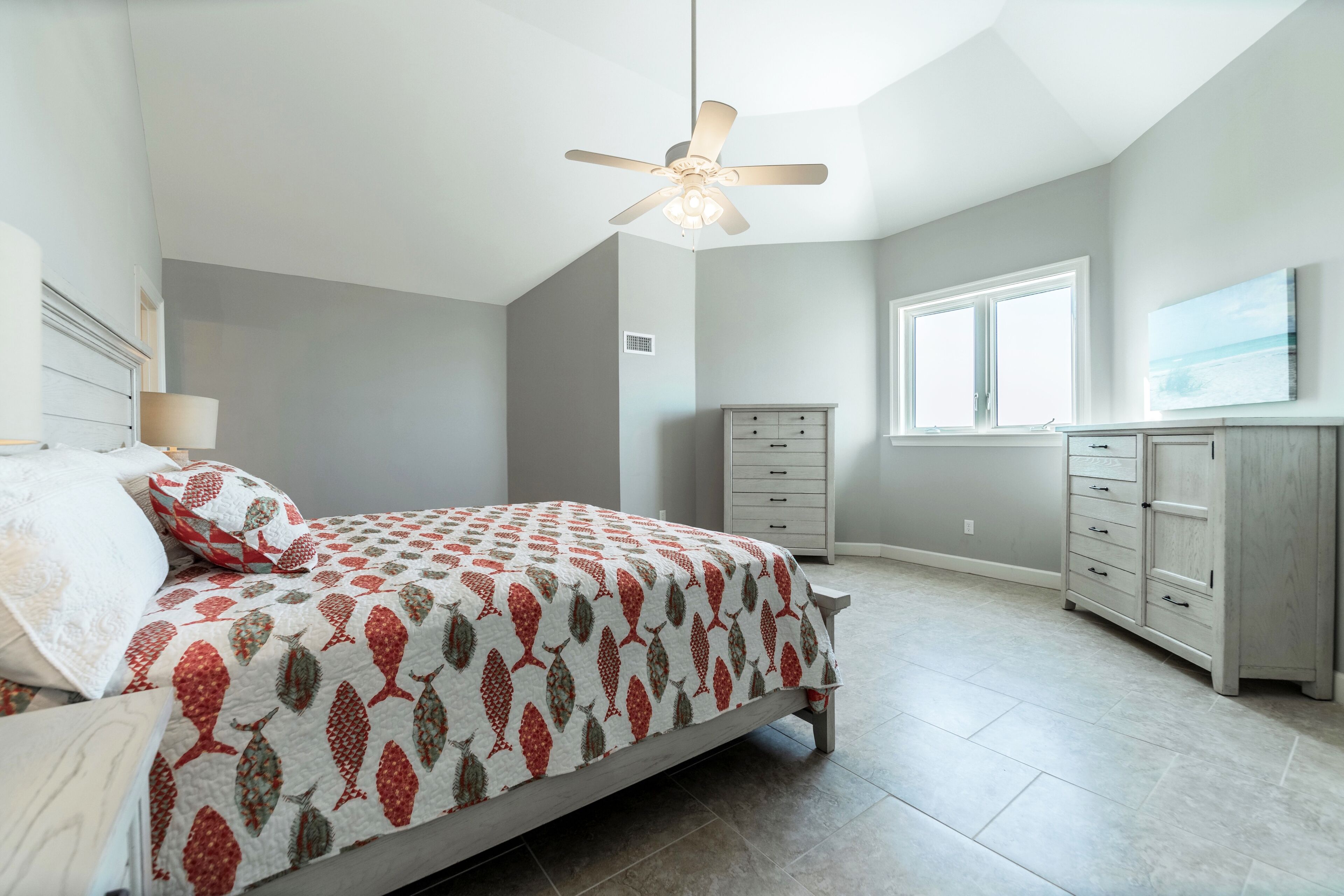Een slaapkamer met een bed, een plafondventilator, een dressoir en een raam.