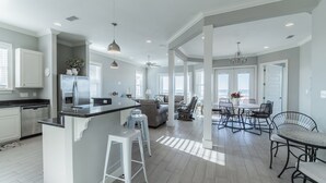 A spacious kitchen with a central island, bar stools, and a dining area with chairs and a table. - Beachy Keen | Late October openings. Pool, gulf front, pets (Dauphin Island)