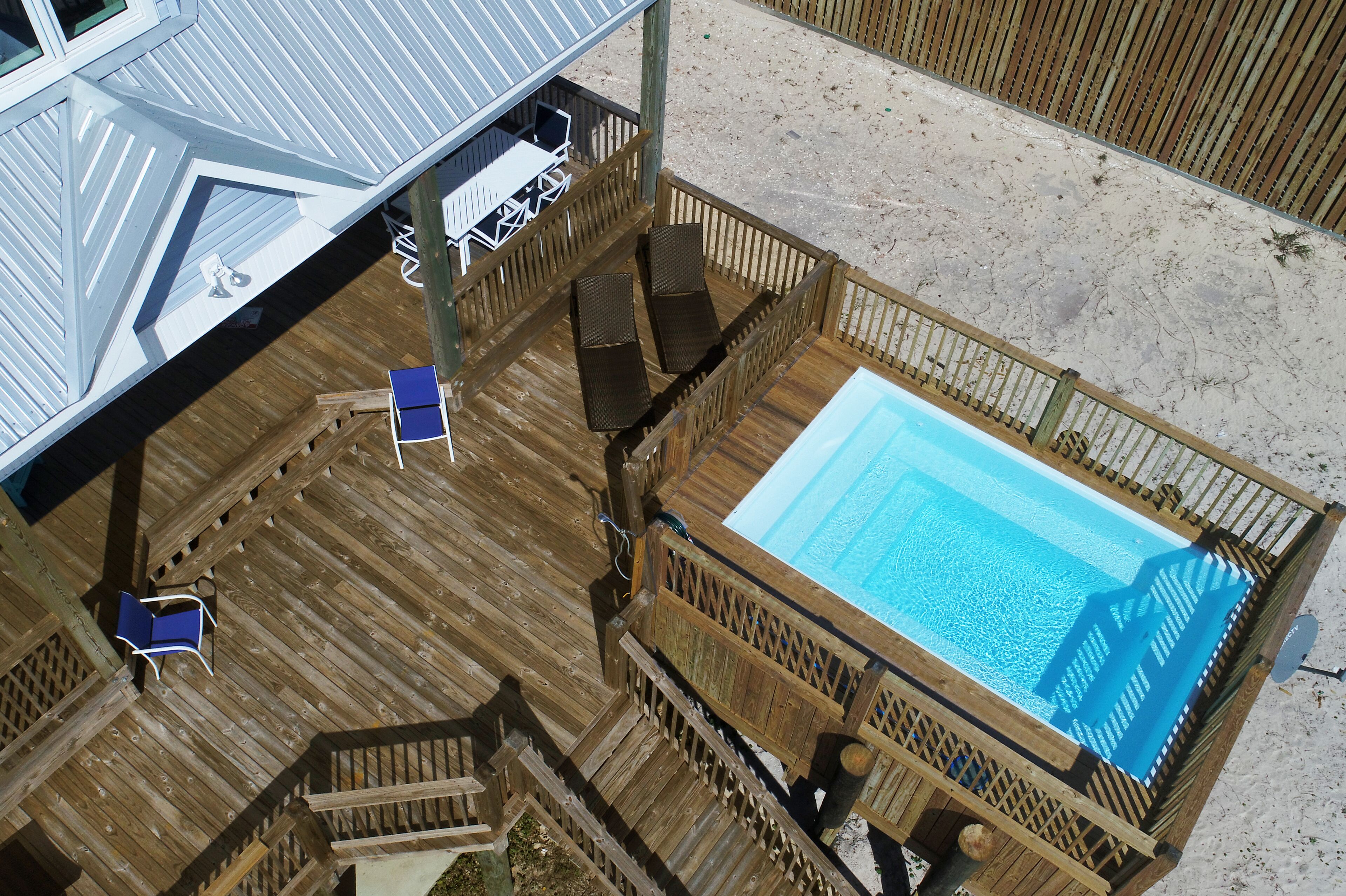 Una terraza de madera con piscina, mobiliario exterior y una zona cubierta con mesa y sillas.