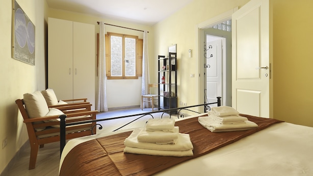 A hotel room with a bed, a wooden bench, a wardrobe, a mirror, and a window. - At 4 for you (Florence)