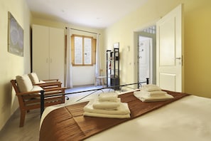 A hotel room with a bed, a wooden bench, a wardrobe, a mirror, and a window.