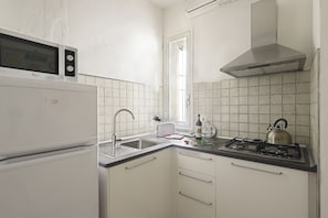 A compact kitchen with a built-in microwave, a sink, a toaster, a gas stove, and a stainless steel kettle.