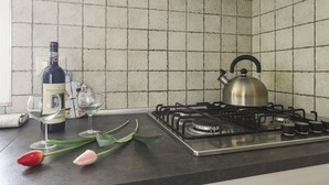 A kitchen with a gas stove, a kettle, a wine bottle, and two wine glasses. - At 4 for you (Florence)