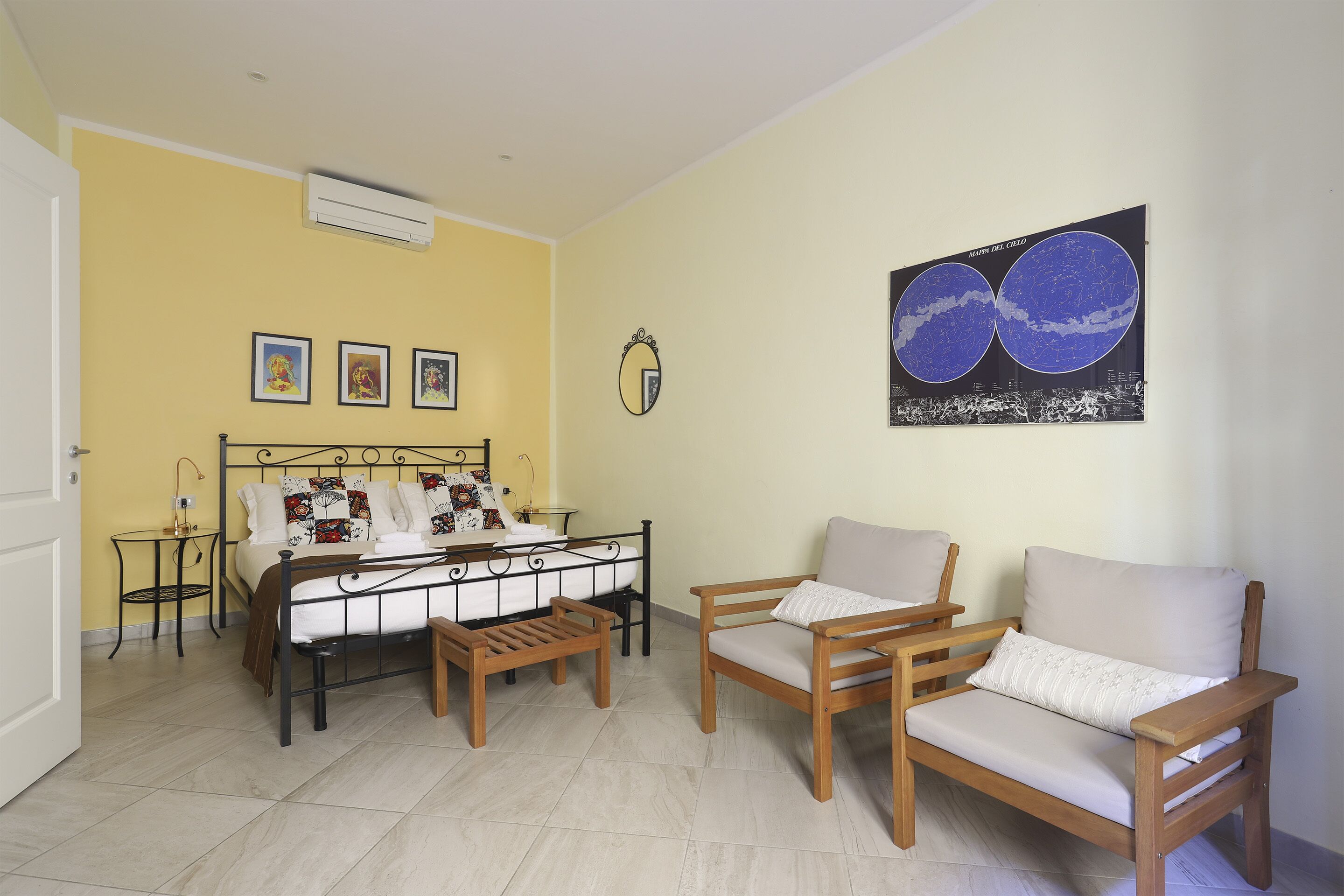 A bedroom with a bed, two wooden chairs, a small table, and a wall-mounted air conditioner.