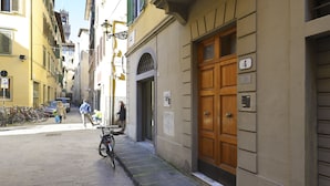A narrow street with a building featuring a large wooden door and a sign indicating room number 4. - At 4 for you (Florence)