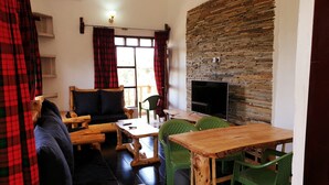 Un área de estar acogedora con un sofá, una mesa de centro de madera y sillas de plástico verde. Un televisor de pantalla plana está montado en una pared de piedra.