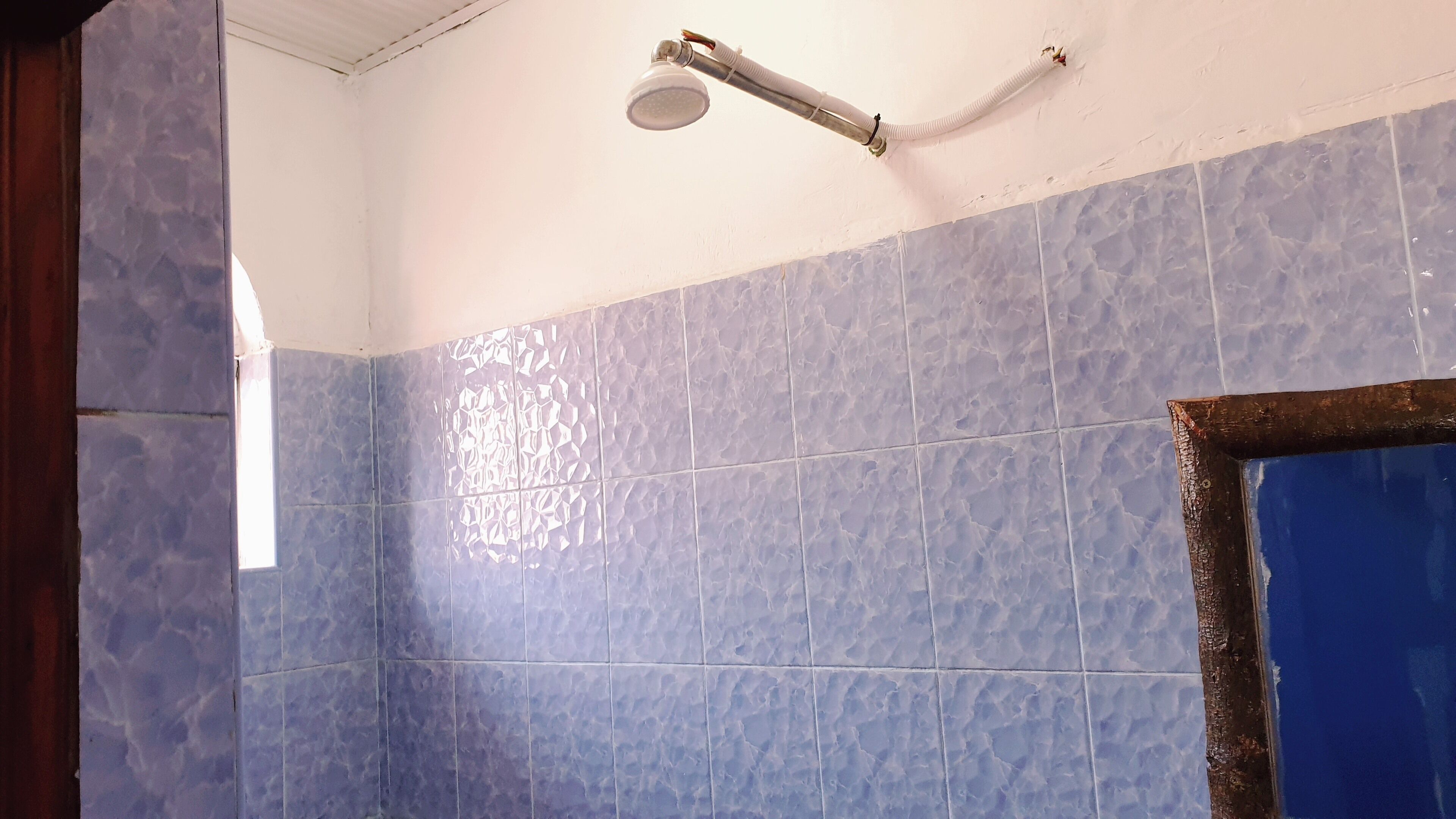 A bathroom with blue tiles, a showerhead, and a partially visible door frame.