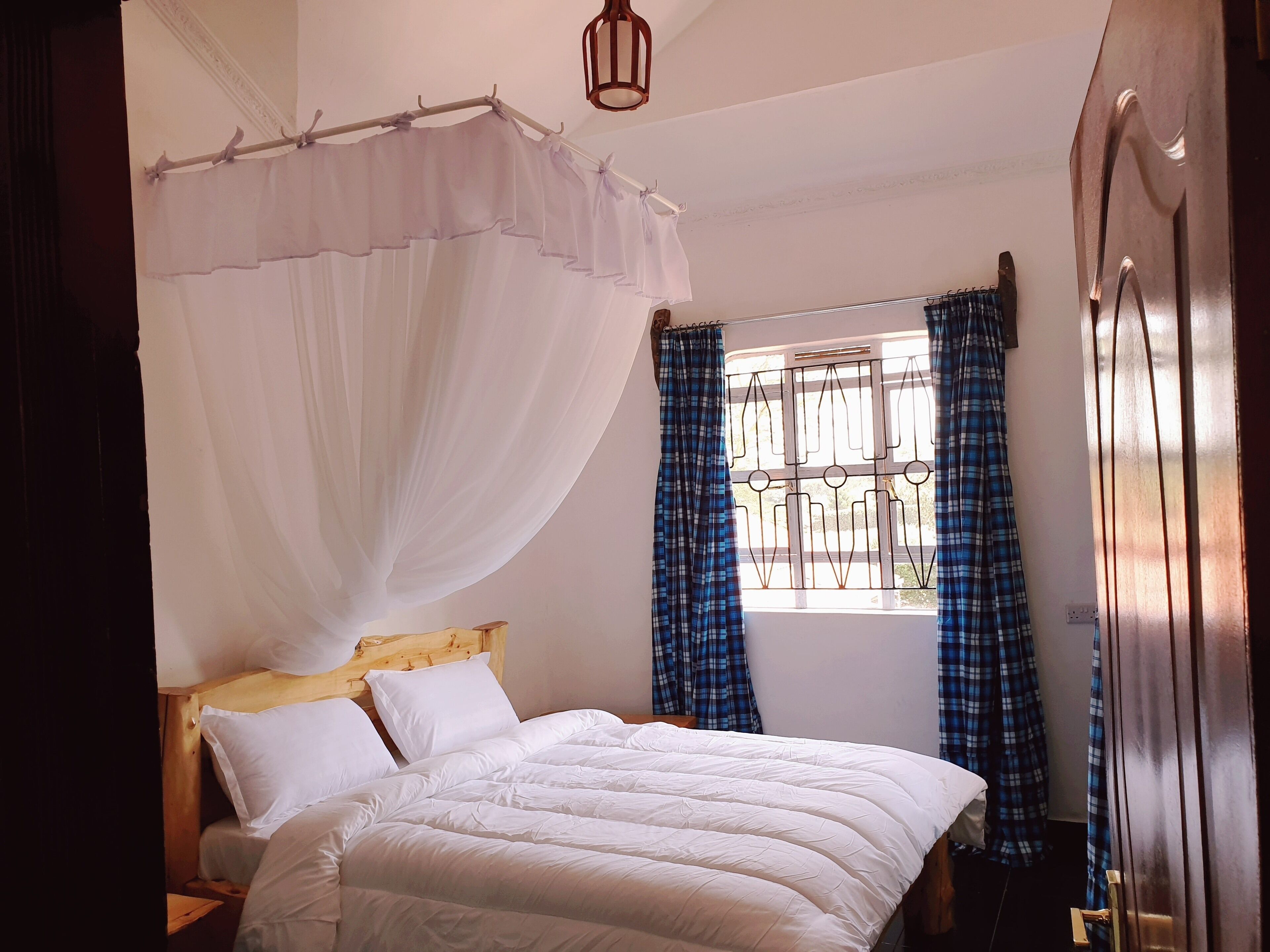 A bedroom with a bed, a wooden headboard, a window with metal bars, and a door.