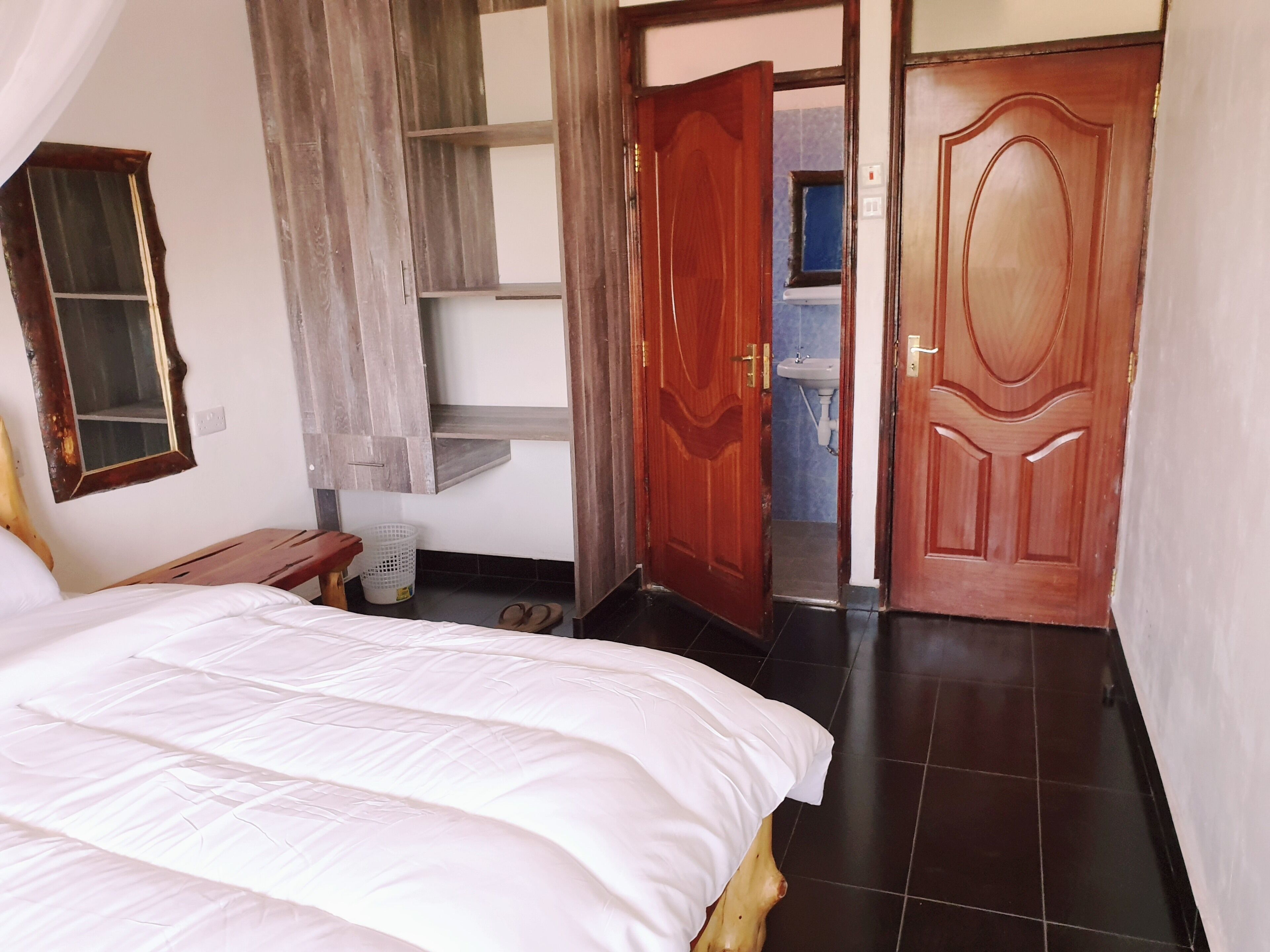 Una camera da letto con un letto, un armadio in legno, uno specchio e un bagno visibile tramite una porta aperta.