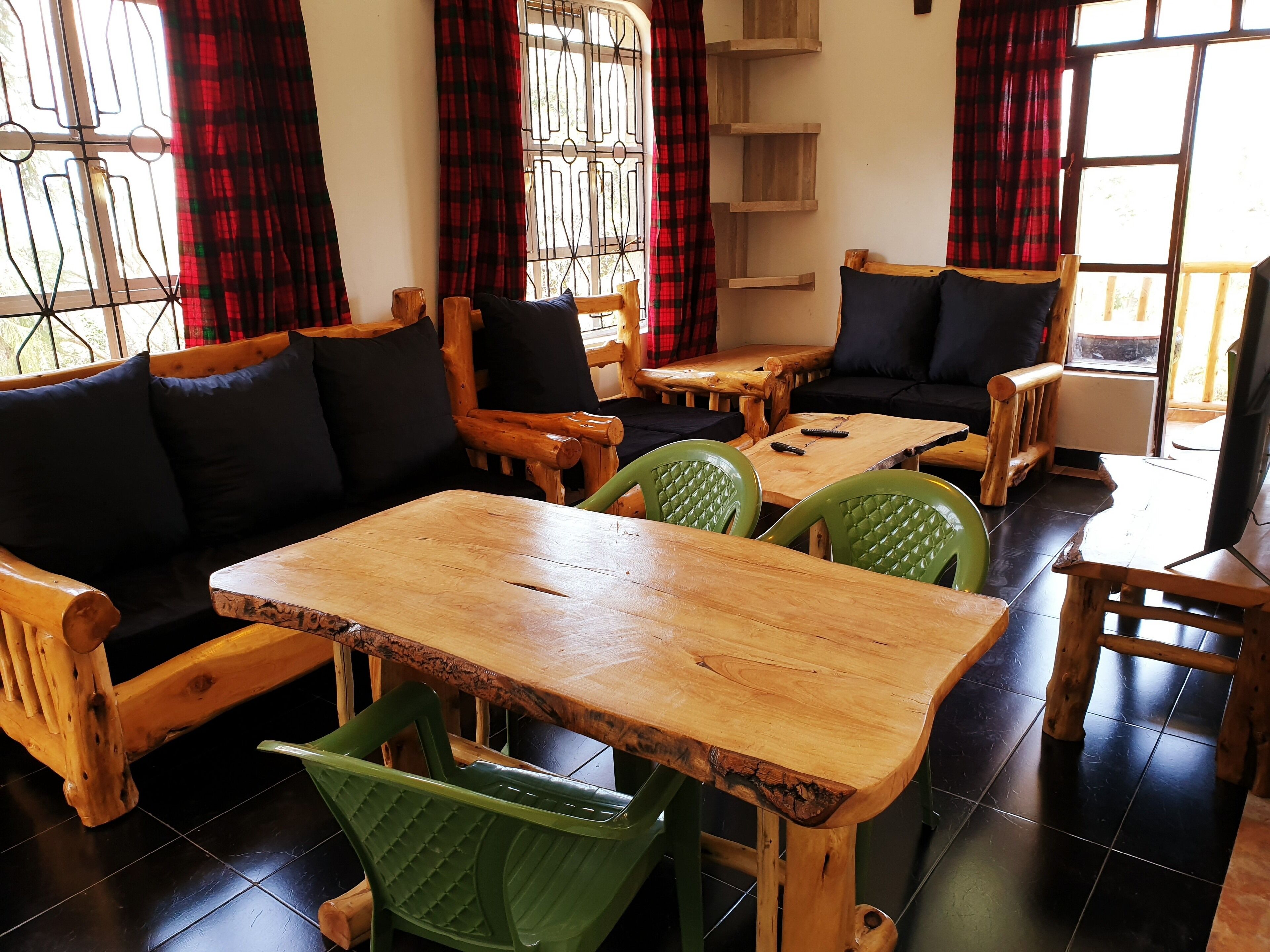 Une pièce chaleureuse avec une table et des chaises en bois, un canapé avec des coussins noirs et une fenêtre ornée de barreaux en métal et de rideaux rouges.