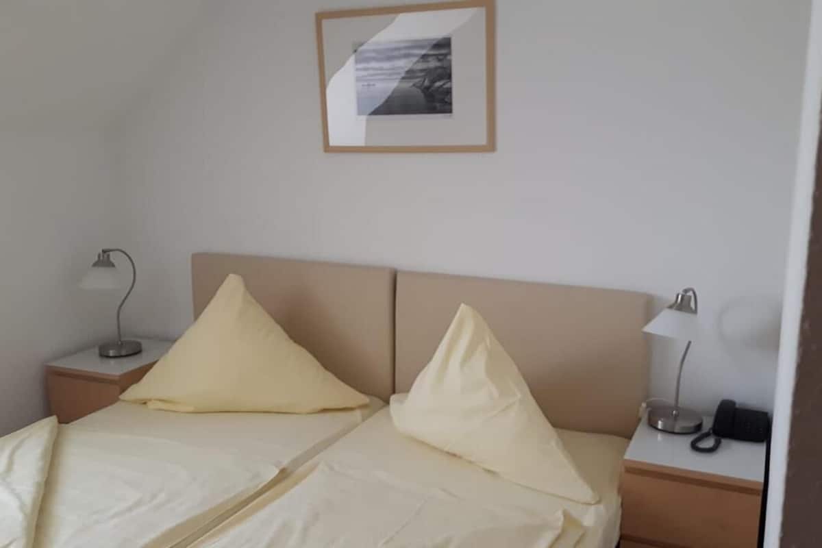 Una cama doble con dos almohadas, una mesita de noche con lámpara y un cuadro enmarcado en la pared.