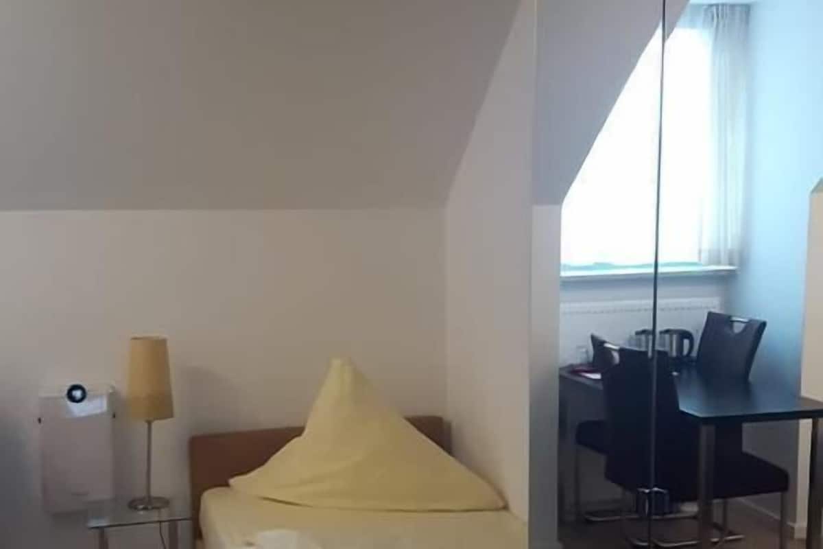 Un dormitorio con cama, mesita de noche, lámpara y vista a un comedor a través de un separador de vidrio.