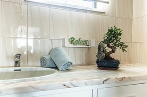 Une salle de bain avec un lavabo en marbre, une serviette, un bonsaï et un panneau « Détendez-vous » accroché au mur.