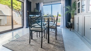 Une salle à manger située à l’étage, avec une table dressée pour quatre personnes, une grande fenêtre avec des rideaux et une vue sur l’extérieur.