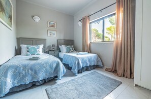 A bedroom with two beds, a window with curtains, a nightstand, and a rug.