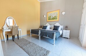 Une chambre à coucher avec un lit, des tables de chevet, une commode, une chaise, un miroir et un tableau accroché au mur.
