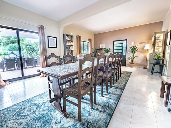 A dining area with a large table and chairs, a patterned rug, and a view through a glass door to an outdoor patio.