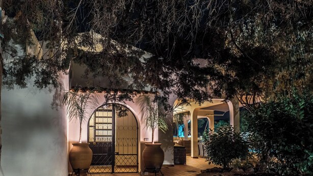 Une entrée en soirée avec un chemin pavé, un grand arbre et un bâtiment doté d’une porte en arc de cercle.