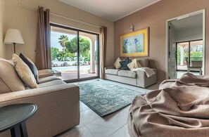 A modern living room with a sofa, a coffee table, and a view of a pool and greenery outside. - Quinta Pequena is a large traditional family villa near Vale Do Lobo (Almancil)