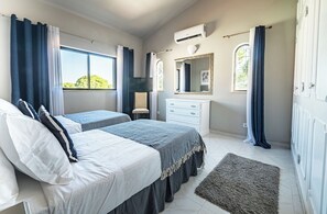 Une chambre avec deux lits, une commode, un miroir et une fenêtre avec des rideaux.
