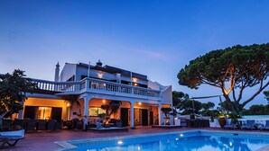 Un bâtiment à deux étages doté d’une piscine, d’un espace extérieur aménagé et d’un grand arbre.