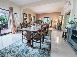 Un comedor amplio con una mesa de mármol y sillas de madera, rodeado de estanterías y plantas en macetas.