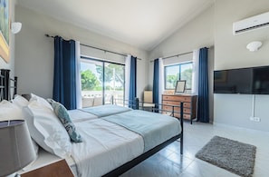 A bedroom with a bed, a dresser, a television, and a view of the outdoors.