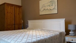 Une chambre à coucher avec un lit, une armoire en bois, un tableau au mur et une table de chevet avec une lampe.