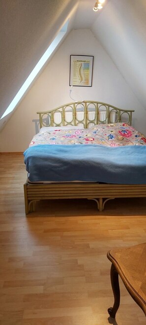 A bedroom with a sloped ceiling, a bed with a floral bedspread, and a framed chart on the wall.