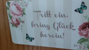 Une carte ornée de motifs floraux et de papillons, sur laquelle on peut lire le texte : « Entrez, apportez la chance ! »