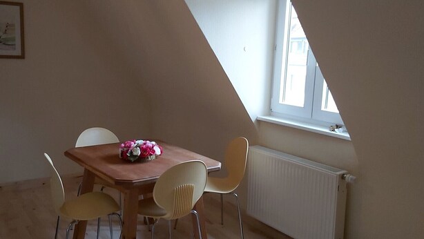 Un coin repas avec une table en bois et quatre chaises, un arrangement floral en guise de décoration centrale et une fenêtre donnant sur un paysage agréable.