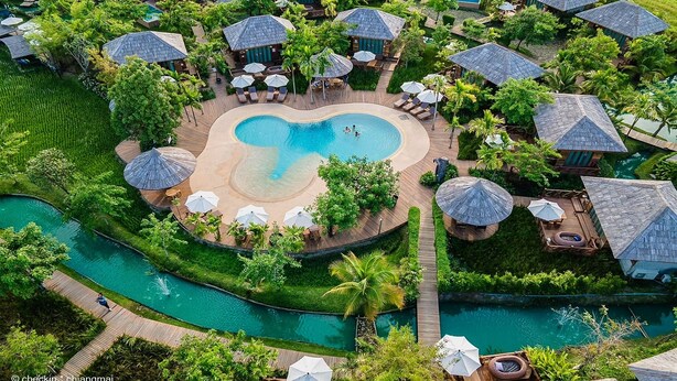 Vue aérienne d’un complexe hôtelier doté d’une piscine centrale, de plusieurs hébergements de type bungalow et d’un paysage luxuriant environnant.