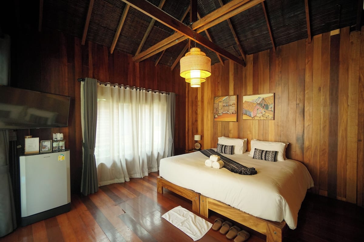 A wooden-paneled room with a bed, a small refrigerator, a television, and a hanging light fixture.