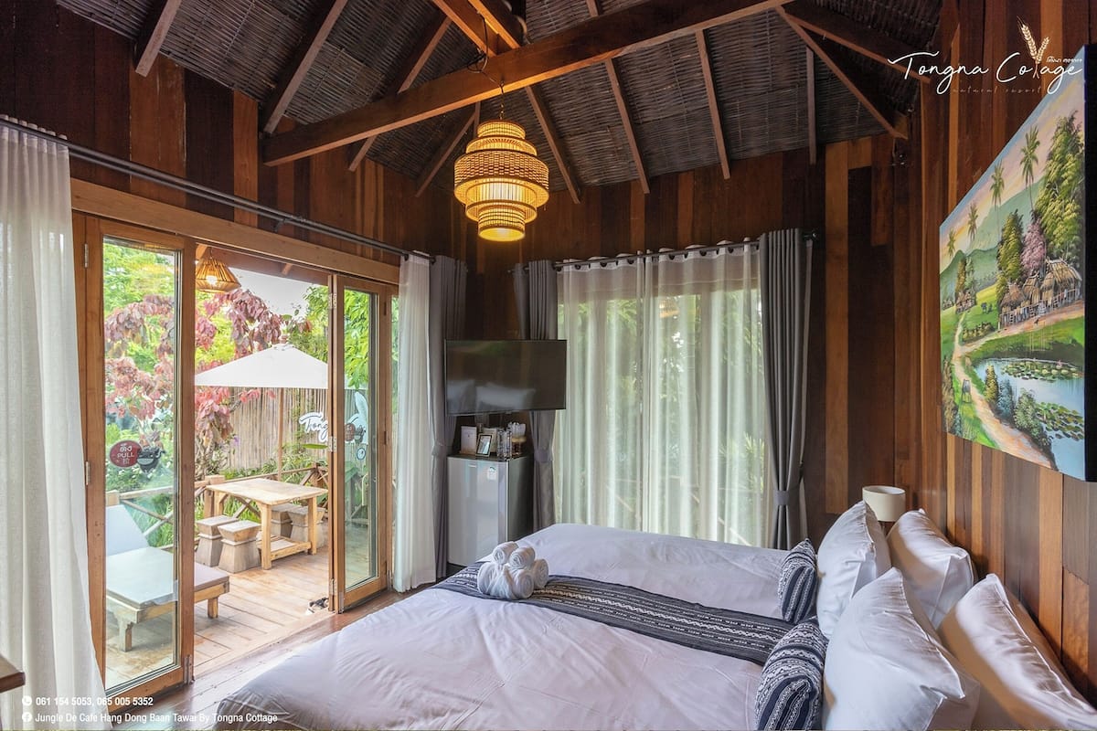A bedroom with a large bed, a TV, and a sliding glass door leading to an outdoor area with a table and chairs.
