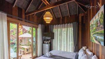 A bedroom with a bed, a television, a refrigerator, and a sliding glass door leading to an outdoor area with a table and chairs.