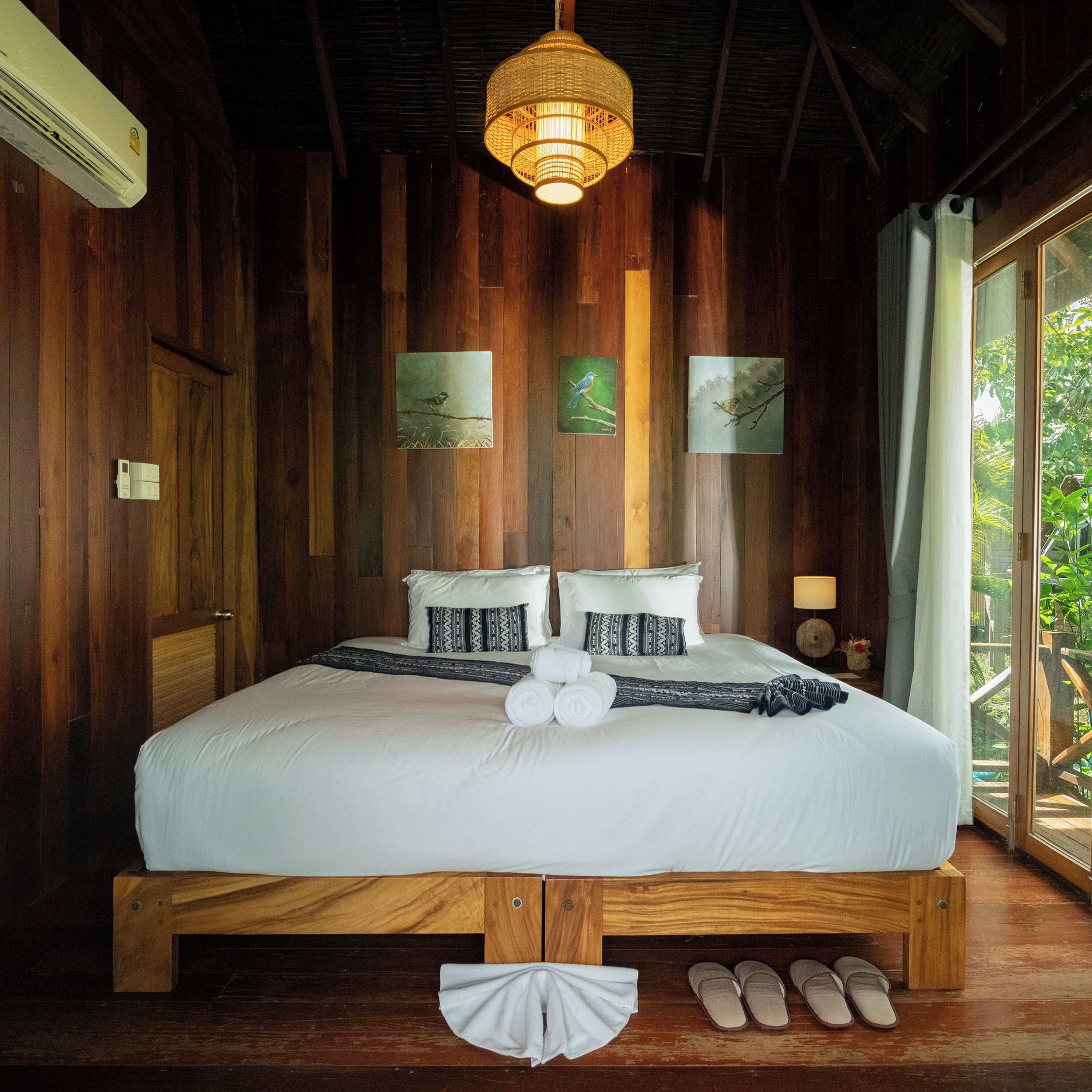 A wooden-framed bed with white bedding, a hanging light fixture, and two framed pictures on the wall.