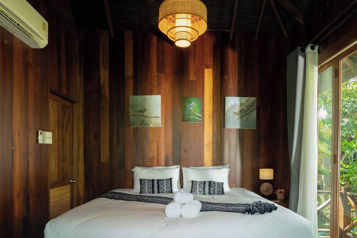 Een bed met houten frame, witte beddengoed, een hanglamp en twee ingelijste foto’s aan de muur.