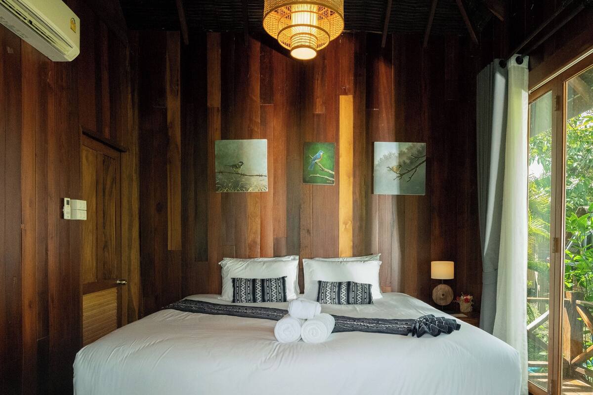 A wooden-framed bed with white bedding, a hanging light fixture, and two framed pictures on the wall.