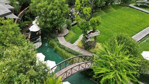 Un jardin luxuriant avec un pont en bois enjambant un bassin, entouré d’arbres et d’une pelouse.