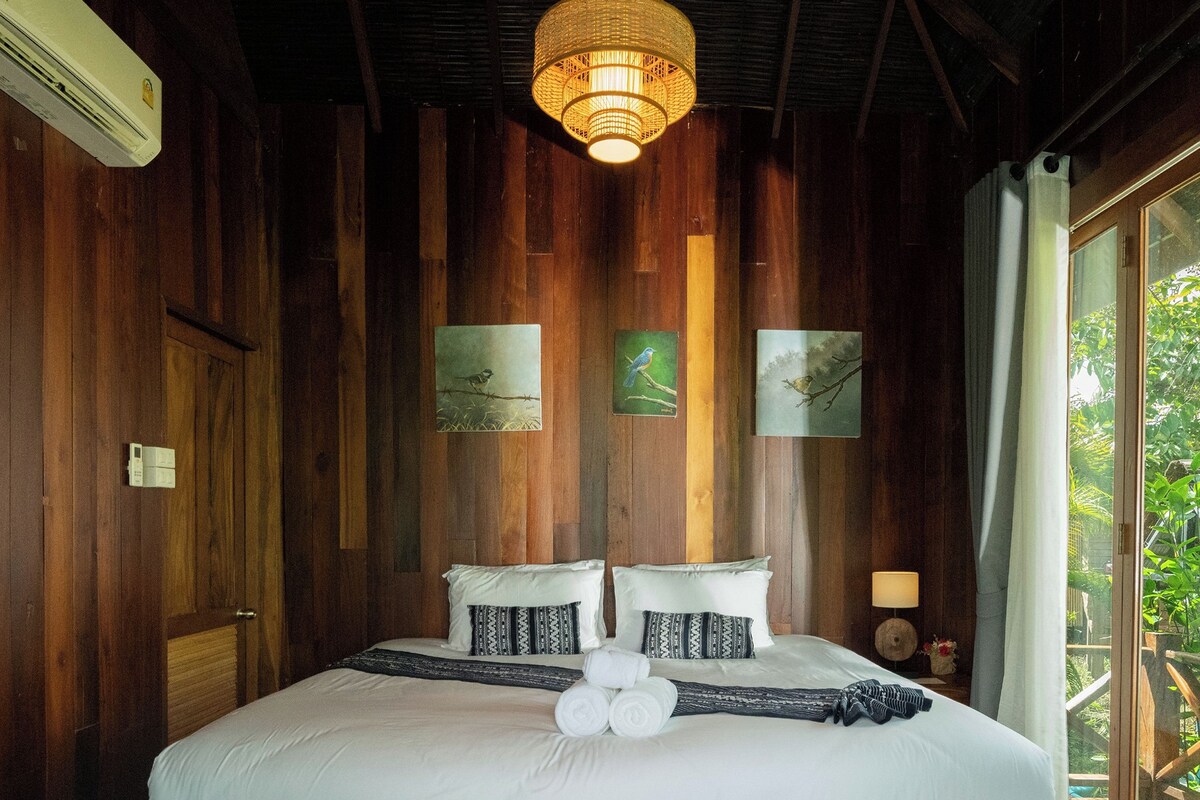 Een bed met houten frame, witte beddengoed, een hanglamp en twee ingelijste foto’s aan de muur.