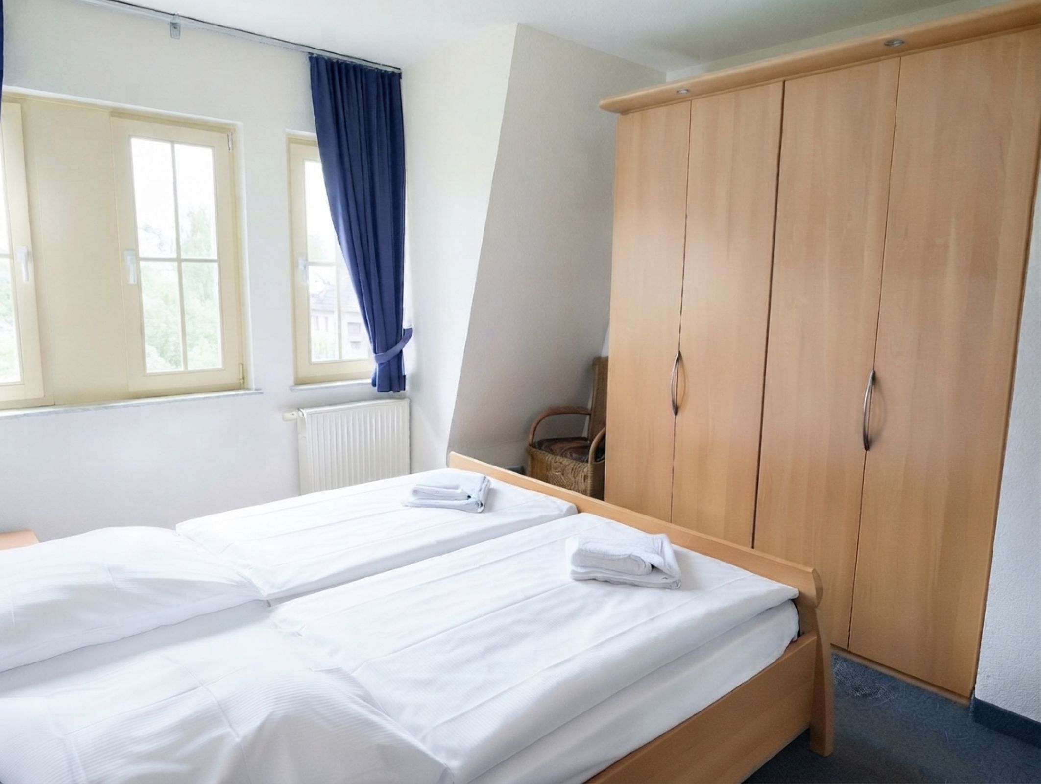 Ein Hotelzimmer mit zwei Betten, einem Kleiderschrank, einer Heizung und einem Fenster mit Vorhängen.